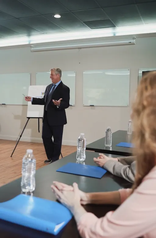 Dozent in Business-Seminar erklärt Inhalte an Flipchart vor Teilnehmern in einem modernen Schulungsraum, Fokus auf Weiterbildung und Krisenmanagement-Training.